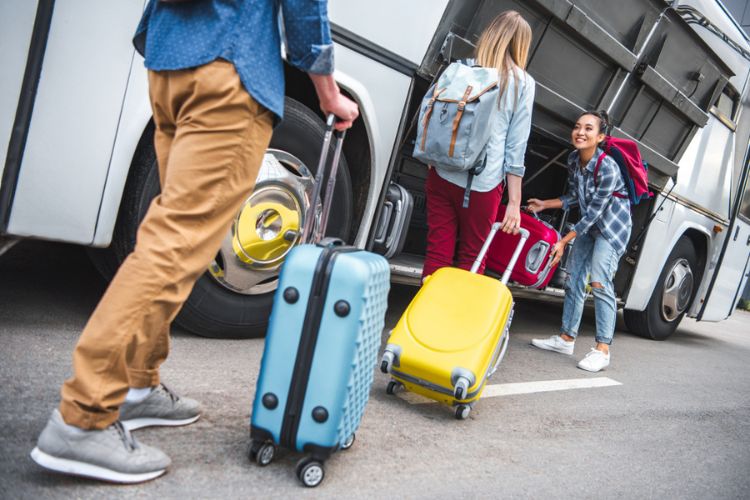 Travelers loading personal belongings into a charter bus luggage bay.